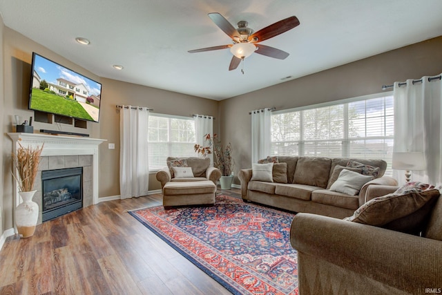 living area featuring wood finished floors, baseboards, recessed lighting, a tiled fireplace, and a ceiling fan
