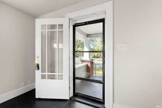 doorway to outside featuring baseboards and lofted ceiling
