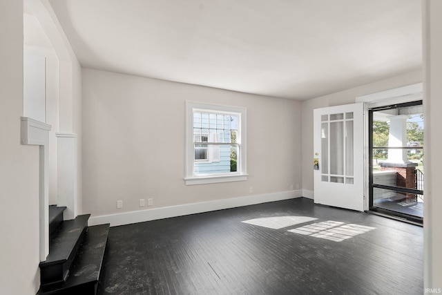 unfurnished living room with baseboards, dark wood-type flooring, and a wealth of natural light