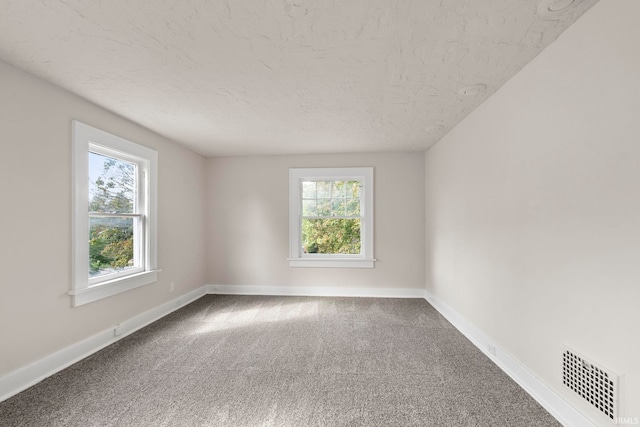 empty room with visible vents, a textured ceiling, carpet floors, and baseboards