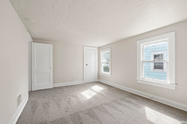 spare room featuring carpet flooring, a textured ceiling, visible vents, and baseboards