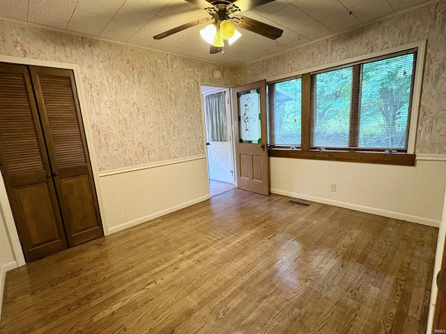 unfurnished bedroom featuring a closet, visible vents, wainscoting, wood finished floors, and a ceiling fan