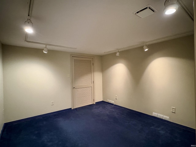 unfurnished room featuring track lighting, dark carpet, and visible vents