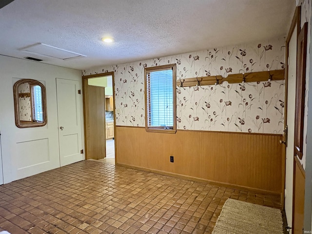 spare room with a textured ceiling, visible vents, wainscoting, wood walls, and wallpapered walls