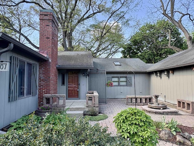 view of exterior entry featuring a shingled roof, a patio area, and a chimney