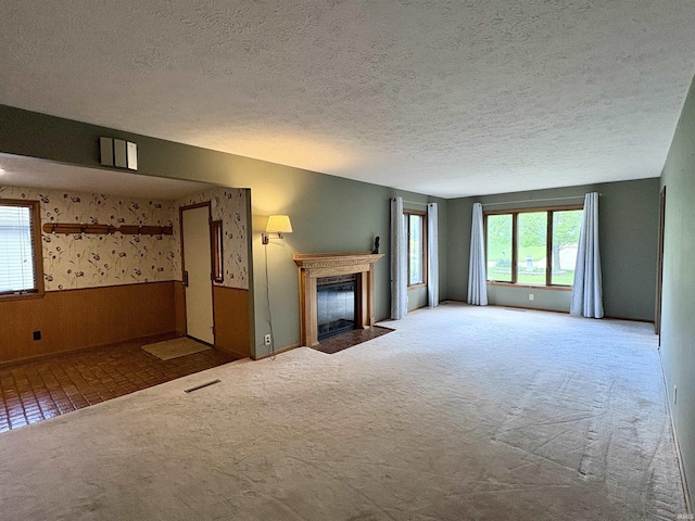 unfurnished living room with a fireplace with flush hearth, carpet flooring, wallpapered walls, and a textured ceiling