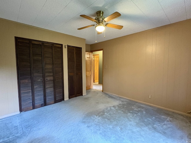unfurnished bedroom featuring carpet floors, a ceiling fan, and two closets