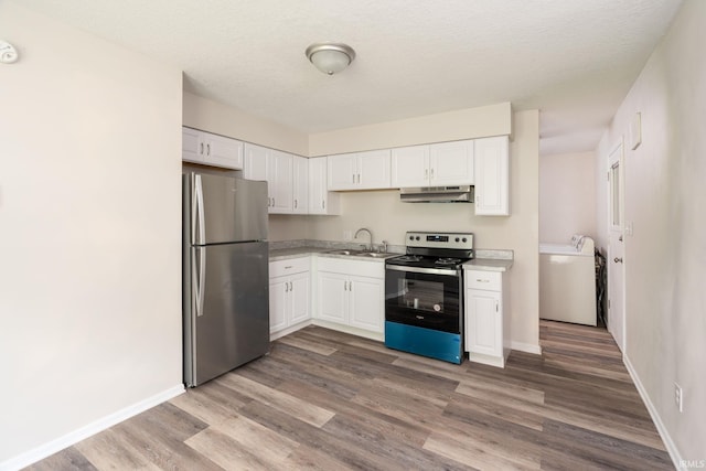 kitchen featuring washer and clothes dryer, white cabinetry, under cabinet range hood, a sink, and stainless steel appliances