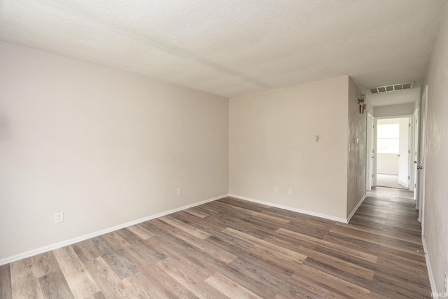 unfurnished room with baseboards, a textured ceiling, wood finished floors, and visible vents