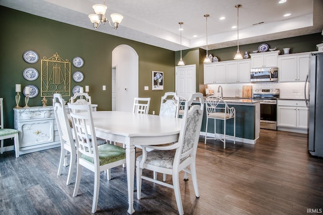 dining space with arched walkways, dark wood finished floors, recessed lighting, and a raised ceiling