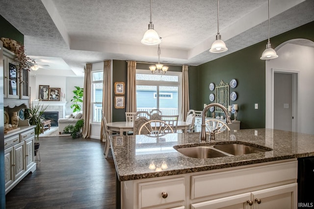 kitchen featuring dark wood-style flooring, a textured ceiling, arched walkways, a sink, and a raised ceiling