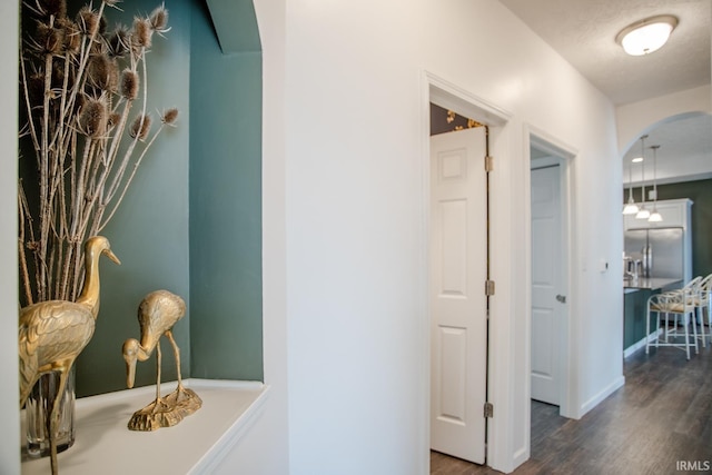 hallway featuring arched walkways, baseboards, and wood finished floors