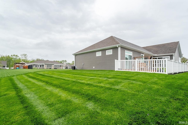 back of property with a lawn, fence, and roof with shingles
