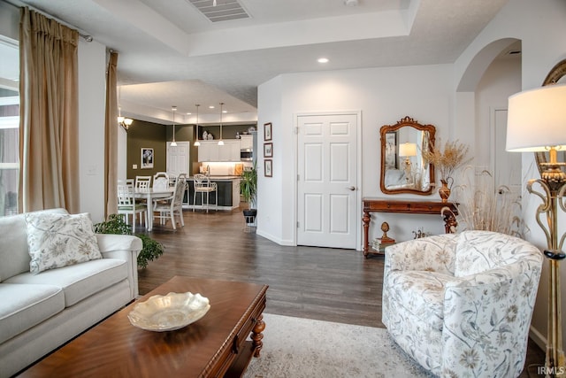 living area featuring visible vents, dark wood-style floors, recessed lighting, a raised ceiling, and arched walkways