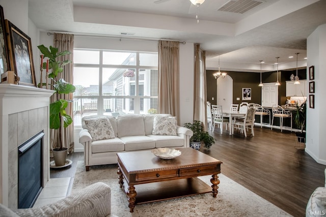 living room with ceiling fan, a raised ceiling, wood finished floors, a tile fireplace, and visible vents