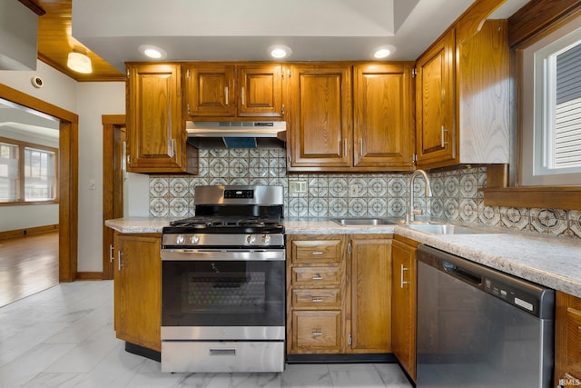 kitchen with brown cabinetry, under cabinet range hood, tasteful backsplash, a sink, and appliances with stainless steel finishes