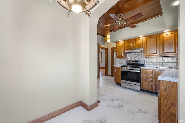 kitchen featuring gas stove, baseboards, under cabinet range hood, and marble finish floor