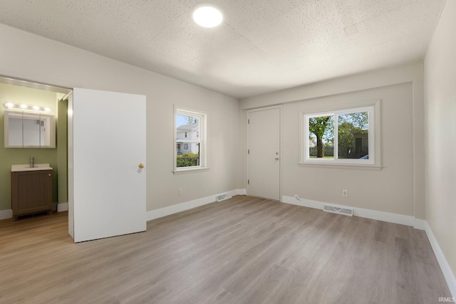 interior space with baseboards, visible vents, a sink, and light wood-style flooring