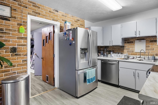 kitchen with a sink, light wood-style floors, light countertops, brick wall, and stainless steel appliances