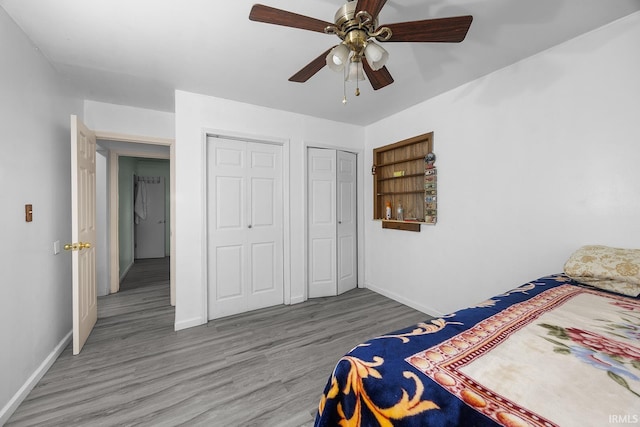bedroom featuring baseboards, a ceiling fan, multiple closets, and wood finished floors