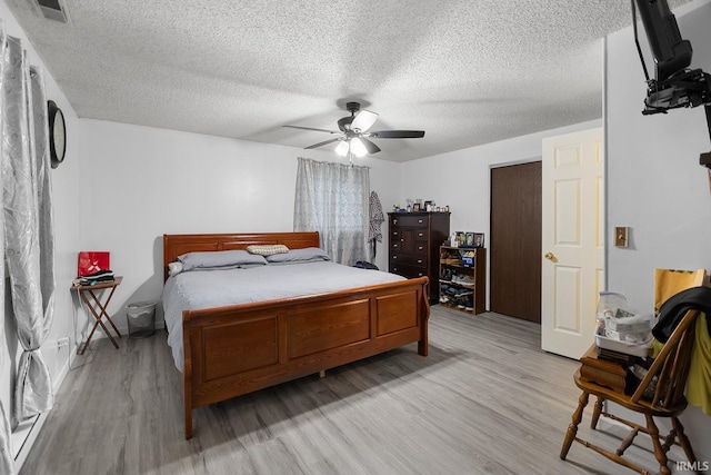 bedroom featuring visible vents, a textured ceiling, light wood-style flooring, and a ceiling fan