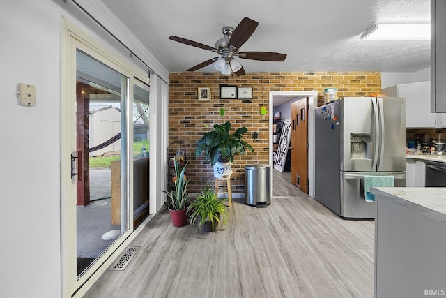 kitchen featuring brick wall, stainless steel fridge, light countertops, a ceiling fan, and light wood finished floors