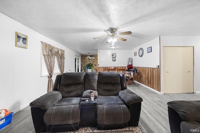 living area with ceiling fan, a textured ceiling, wood walls, a wainscoted wall, and wood finished floors