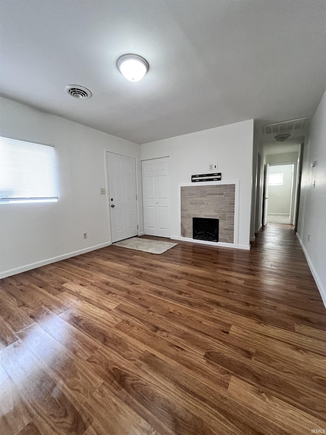 unfurnished living room featuring baseboards, visible vents, wood finished floors, and a fireplace