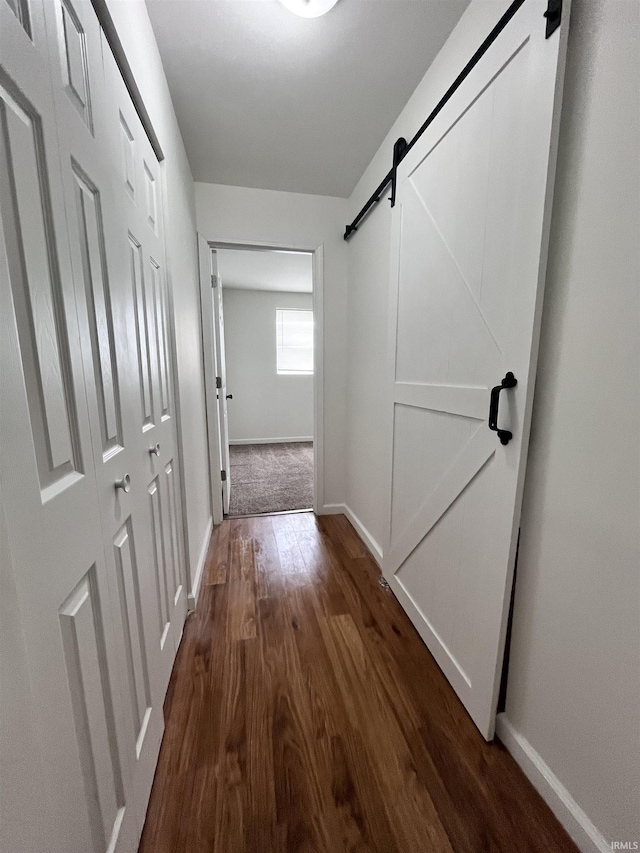 hallway featuring baseboards, a barn door, and dark wood-type flooring