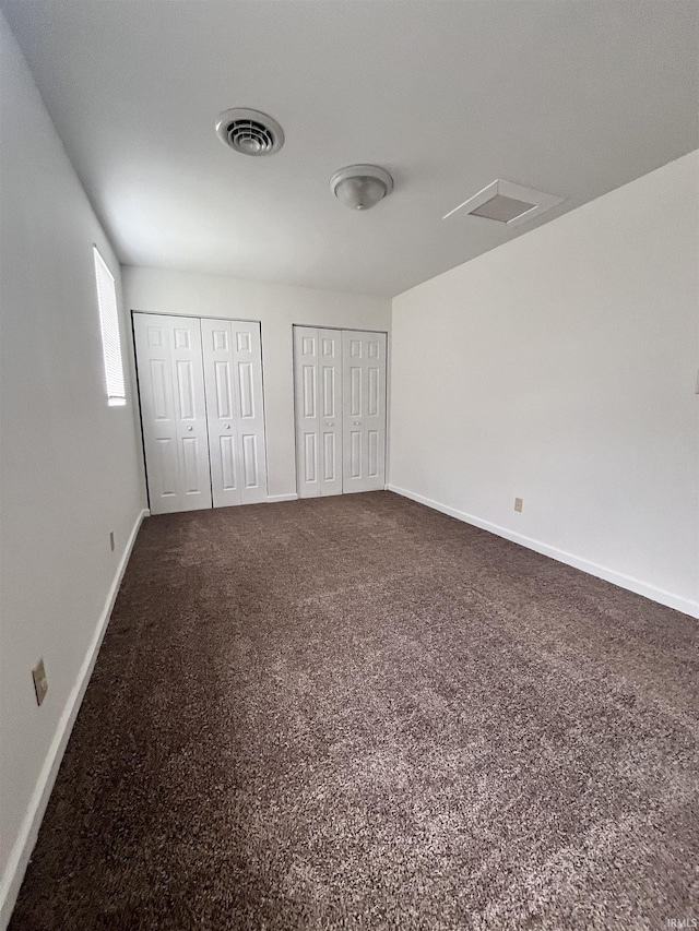 unfurnished bedroom with two closets, baseboards, visible vents, and dark carpet