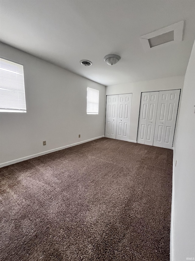 unfurnished bedroom featuring visible vents, two closets, baseboards, attic access, and carpet