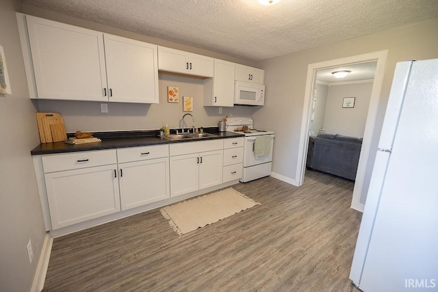 kitchen with dark countertops, white appliances, white cabinets, a sink, and light wood finished floors