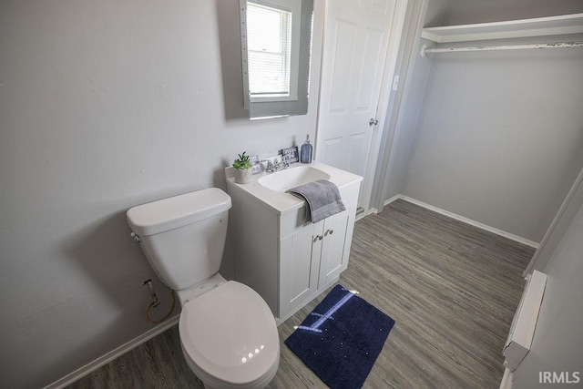 half bath with baseboards, wood finished floors, toilet, and vanity