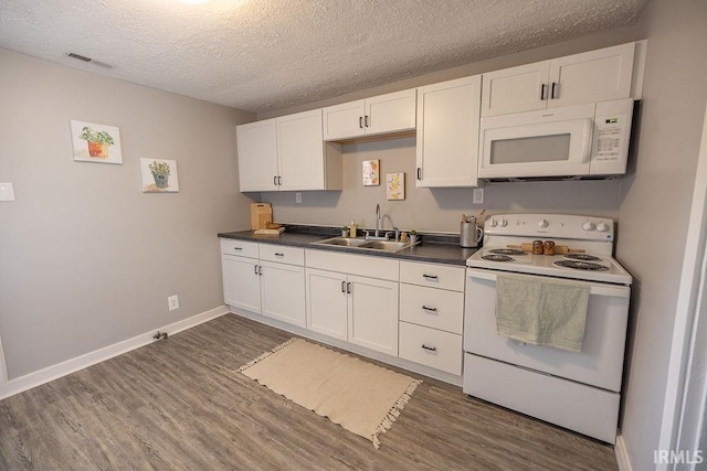 kitchen featuring dark countertops, a sink, white cabinets, white appliances, and dark wood-type flooring