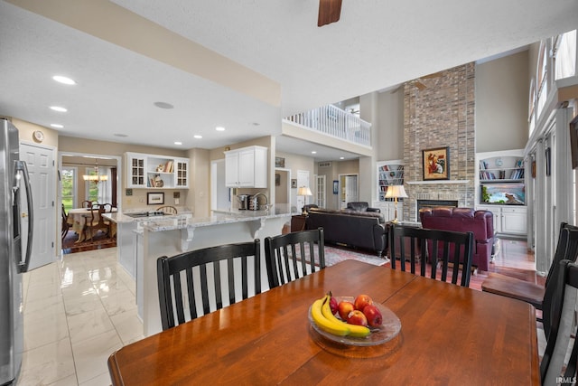 dining area featuring a towering ceiling, a fireplace, ceiling fan with notable chandelier, marble finish floor, and recessed lighting