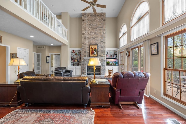 living area featuring wood-type flooring, ceiling fan, visible vents, and a towering ceiling