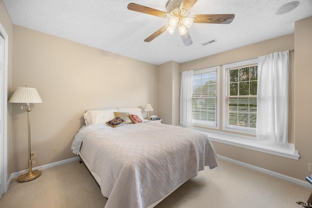 bedroom with a ceiling fan, a textured ceiling, visible vents, baseboards, and carpet flooring
