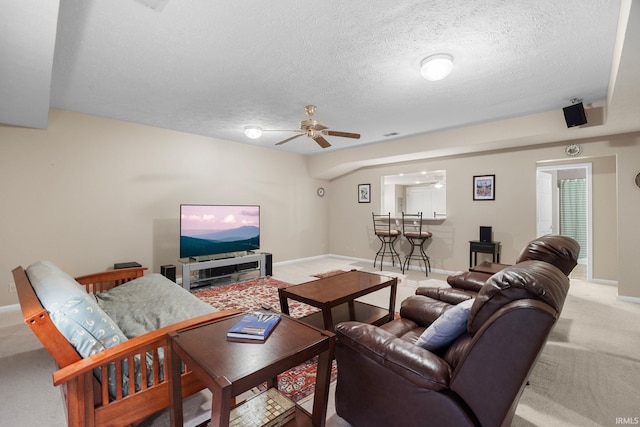 living area with a ceiling fan, a textured ceiling, light carpet, and baseboards