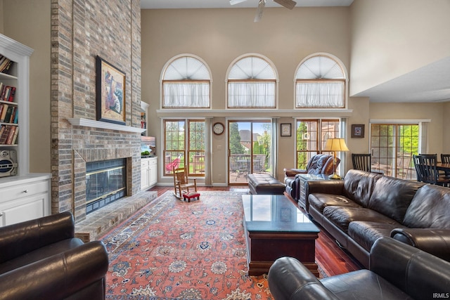 living room featuring wood finished floors, a brick fireplace, ceiling fan, and a high ceiling