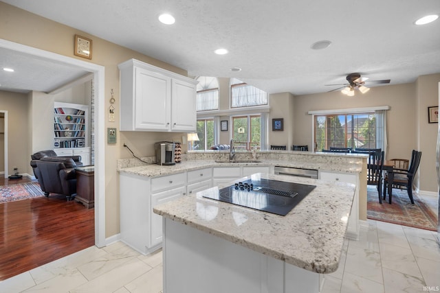 kitchen with black electric stovetop, a sink, marble finish floor, a peninsula, and stainless steel dishwasher