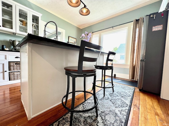 bar featuring crown molding, a textured ceiling, freestanding refrigerator, and wood-type flooring