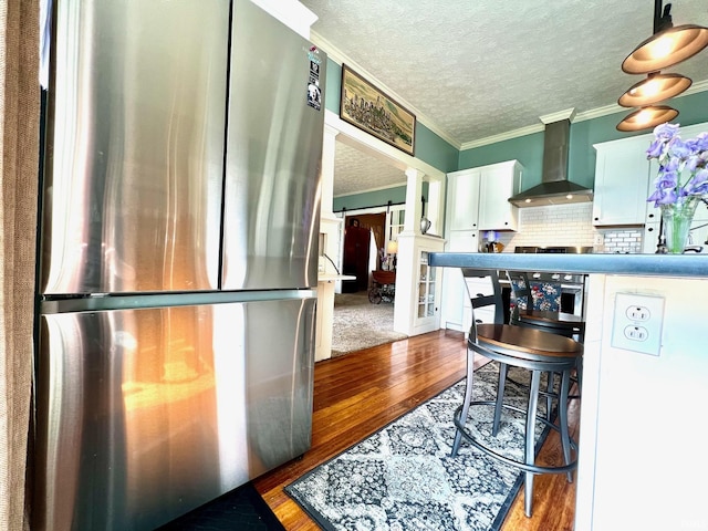 kitchen with crown molding, wall chimney exhaust hood, freestanding refrigerator, ornate columns, and hardwood / wood-style floors