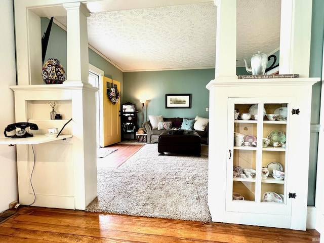 living room featuring ornate columns, ornamental molding, a textured ceiling, and wood finished floors