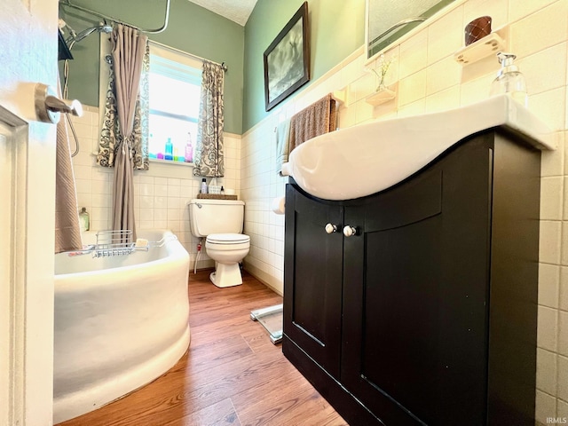 full bath featuring tile walls, wainscoting, wood finished floors, vanity, and toilet