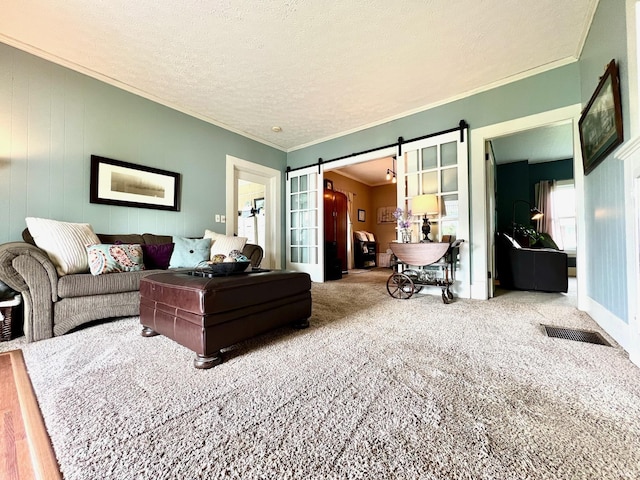 living room with a textured ceiling, visible vents, a barn door, carpet floors, and ornamental molding