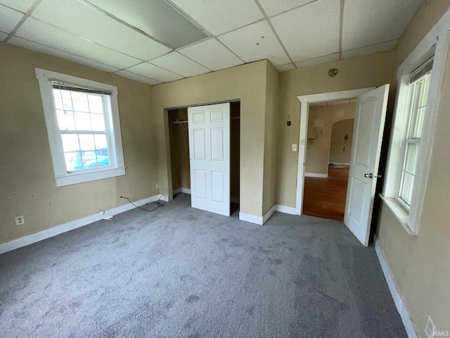 unfurnished bedroom featuring arched walkways, a paneled ceiling, carpet, baseboards, and a closet