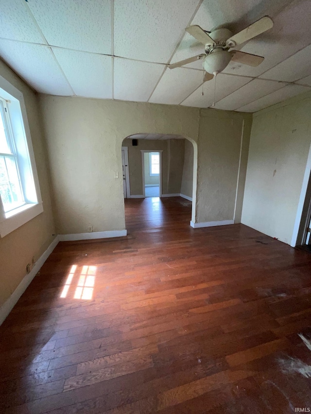 unfurnished room featuring arched walkways, a drop ceiling, ceiling fan, and wood finished floors