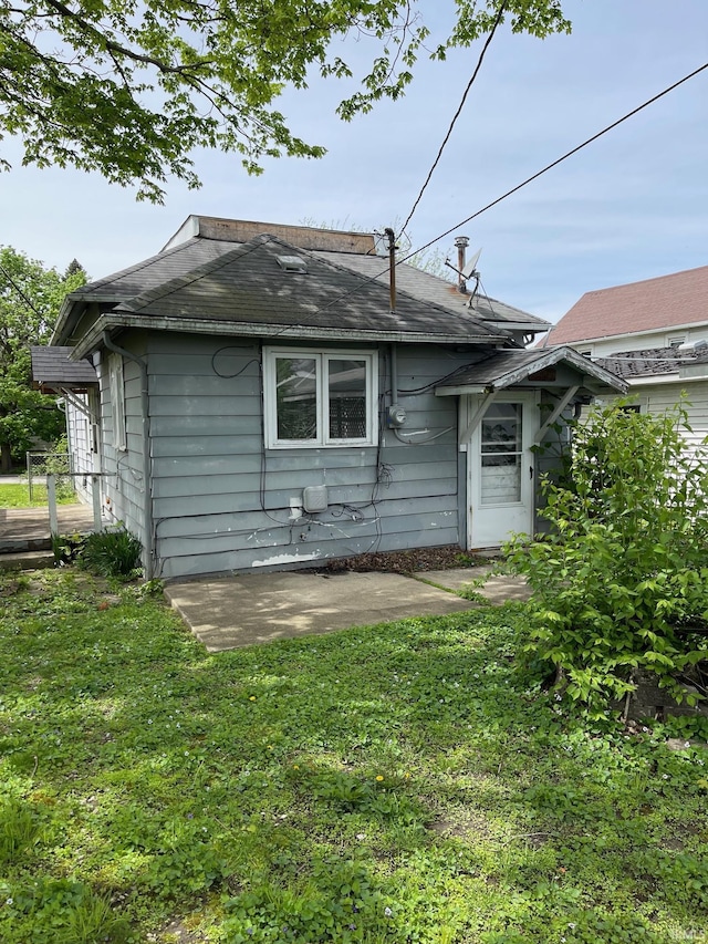 rear view of property with a yard, a shingled roof, and a patio area