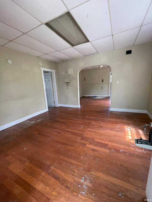 unfurnished room featuring baseboards, arched walkways, a paneled ceiling, and wood finished floors