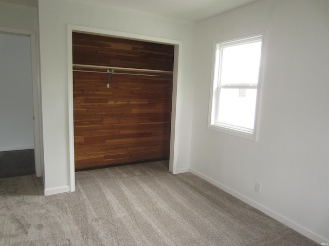 unfurnished bedroom with a closet, carpet, baseboards, and wooden walls